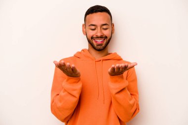 Beyaz arka planda izole edilmiş genç İspanyol bir adam avuçlarıyla bir şey tutuyor ve kameraya sunuyor..