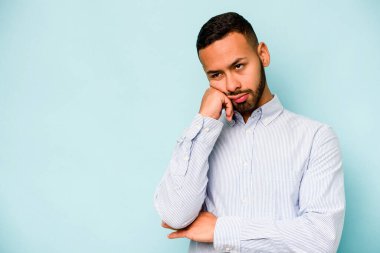 Mavi arka planda izole edilmiş, üzgün ve dalgın hisseden genç bir İspanyol fotokopi odasına bakıyor..