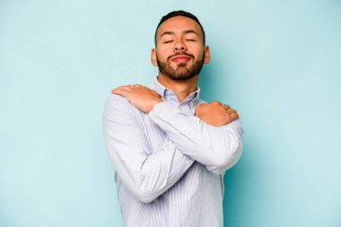 Genç İspanyol adam mavi arka planda yalnızdı. Kucaklaşma, kaygısız gülümseme ve mutluluk..