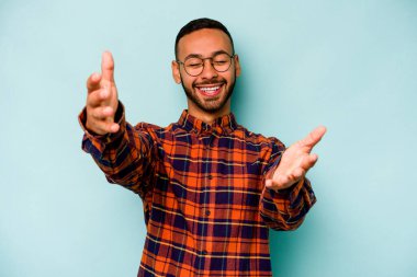 Mavi arka planda izole edilmiş genç İspanyol adam kameraya sarıldığı için kendinden emin hissediyor..