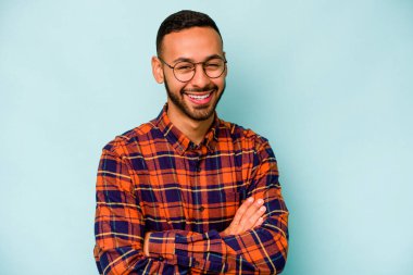 Genç İspanyol adam mavi arka planda izole edilmiş gülüyor ve eğleniyor..