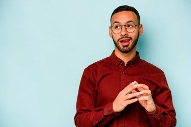 Latin kökenli genç bir adam mavi arka planda izole edildi. Aklında bir plan kuruyor, bir fikir kuruyor..