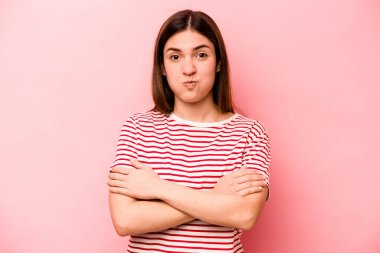 Pembe arka planda izole edilmiş genç beyaz kadın yanakları patlatıyor, yorgun bir ifade takınıyor. Yüz ifadesi kavramı.