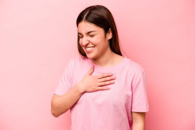 Pembe arka planda soyutlanmış beyaz bir kadın gülüyor, elini yüreğine koyuyor, mutluluk kavramını koruyor..