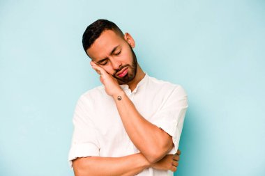 Genç İspanyol adam mavi arka planda izole edilmiş. Tekrarlanan bir görevden yorulmuş..