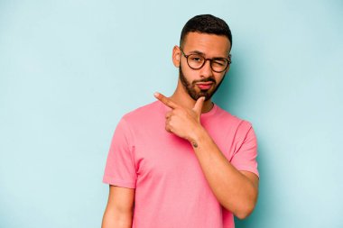 Latin kökenli genç bir adam mavi arka planda izole edilmiş. Bir strateji planlıyor, bir iş yolu düşünüyor..