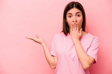 Pembe arka planda izole edilmiş genç beyaz kadın, avuç içi fotokopi alanını elinde tutmaktan etkilenmiş..