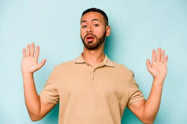 Genç İspanyol bir adam mavi arka planda izole edilmiş. Yakın bir tehlike nedeniyle şok oluyor.