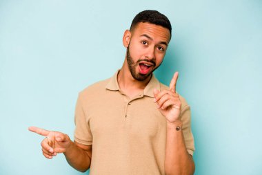 Mavi arka planda izole edilmiş genç İspanyol adam farklı kopya alanlarını gösteriyor, birini seçiyor, parmaklarıyla gösteriyor..