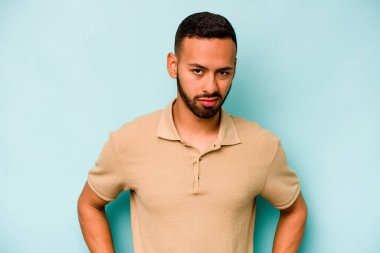 Genç İspanyol adam mavi arka planda izole edilmiş üzgün, ciddi yüz, mutsuz ve hoşnutsuz hissediyor.