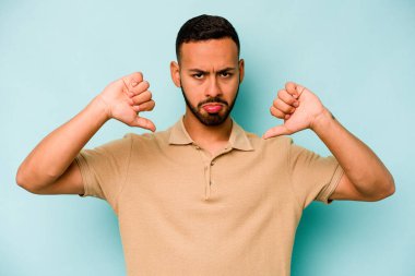 Genç İspanyol bir adam mavi arka planda izole edilmiş. Hoşlanmadığı bir hareket gösteriyor. Anlaşmazlık konsepti.