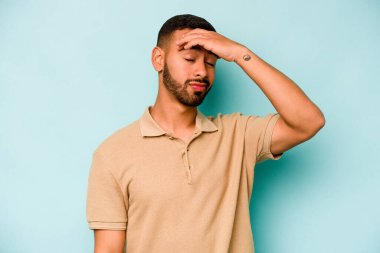 Genç İspanyol adam mavi arka planda izole edilmiş tapınaklara dokunuyor ve baş ağrısı çekiyor..
