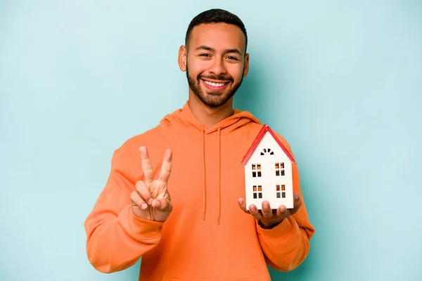 Young Hispanic Man Holding Toy House Isolated Blue Background Showing — Stock Photo, Image
