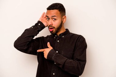 Latin kökenli genç bir adam beyaz arka planda bir dedikoduyu dinlemeye çalışıyor..