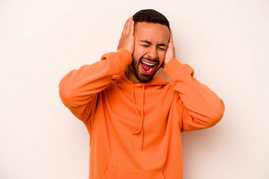 Latin kökenli genç adam beyaz arka planda izole edilmiş. Kulakları kulaklarıyla kapatıyor. Çok fazla ses duymamaya çalışıyor..