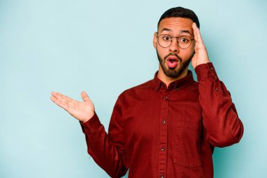 Mavi arka planda izole edilmiş genç İspanyol adam, avuç içinde kopya alanı tutmaktan etkilenmiş..