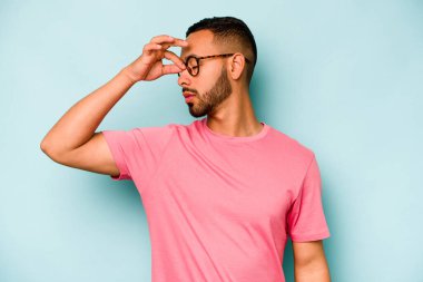 Genç İspanyol bir adam mavi arka planda izole edilmiş, başı ağrıyor, yüzüne dokunuyor..