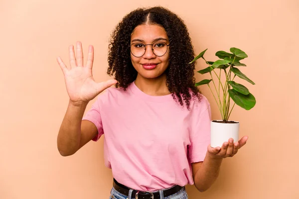 베이지 배경에 고립된 식물을 아프리카계 여성은 손가락으로 번째를 자랑스럽게 — 스톡 사진