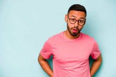 Genç İspanyol bir adam mavi arka planda izole edilmiş. Gördüğü bir şey yüzünden şok oluyor..