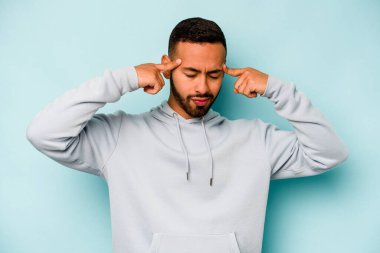 Mavi arka planda izole edilmiş genç İspanyol bir adam bir göreve odaklanmış, işaret parmaklarını işaret ediyor..