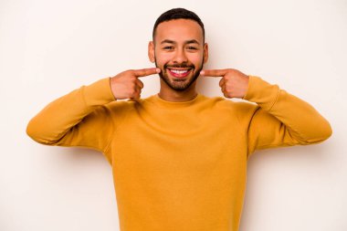 Beyaz arka planda izole edilmiş genç İspanyol adam gülümsüyor, parmaklarını ağıza doğrultuyor..
