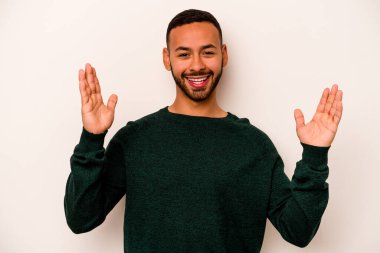 Latin kökenli genç bir adam beyaz arka planda izole edilmiş. Hoş bir sürprizle karşılaşıyor, heyecanlı ve el kaldırıyor..