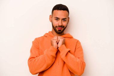 Beyaz arka planda izole edilmiş genç İspanyol adam ellerini çenesinin altında tutuyor ve mutlu bir şekilde yan tarafa bakıyor..