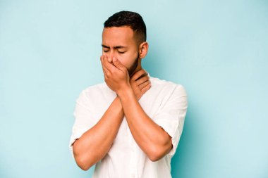 Mavi arka planda izole edilmiş genç İspanyol bir adam virüs ya da enfeksiyon yüzünden boğazında ağrı hissediyor..