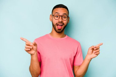 Mavi arka planda izole edilmiş genç İspanyol adam farklı kopya alanlarını gösteriyor, birini seçiyor, parmaklarıyla gösteriyor..