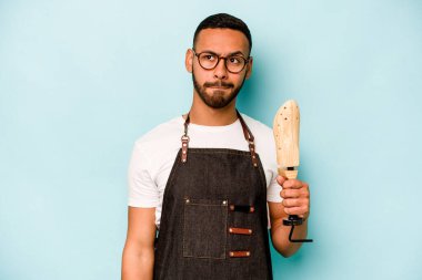 Genç İspanyol kunduracı mavi arka planda izole edilmiş kafası karışmış, şüpheli ve güvensiz hissediyor..