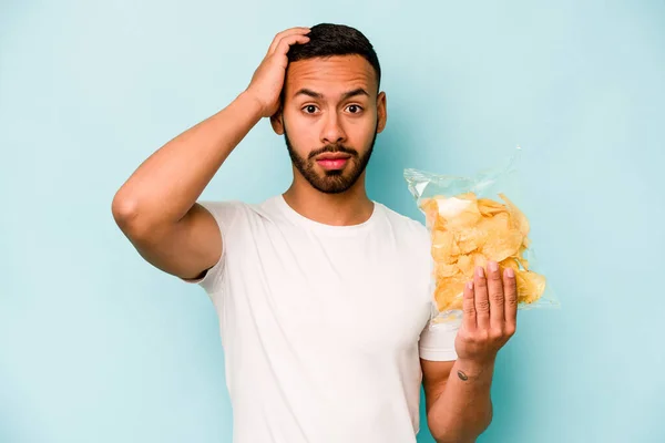 Young Hispanic Man Holding Bag Chips Isolated Blue Background Being — Stock Photo, Image