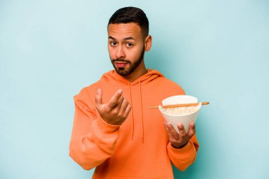 Mavi arka planda izole edilmiş erişte yiyen genç İspanyol kadın sanki seni davet ediyormuş gibi seni işaret ediyor..