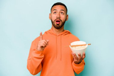 Mavi arka planda izole edilmiş erişte yiyen genç İspanyol kadın ağzı açık bir şekilde üst tarafı işaret ediyor..