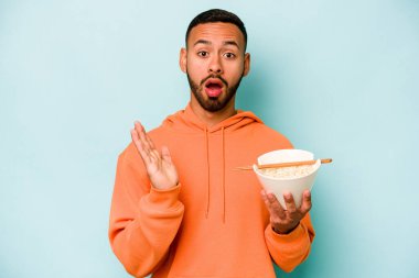 Mavi arka planda izole edilmiş erişte yiyen genç İspanyol kadın şaşırdı ve şok oldu..