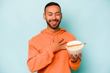 Mavi arka planda izole edilmiş erişte yiyen genç İspanyol kadın elini göğsünde tutarak kahkahalar atıyor..