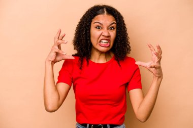 Genç Afrikalı Amerikalı kadın bej arka planda izole edilmiş öfkeyle bağırıyor..