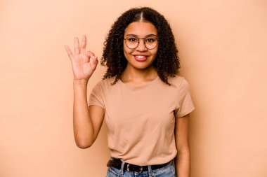 Genç Afrikalı Amerikalı kadın bej arka planda izole edilmiş neşeli ve kendinden emin, iyi bir hareket sergiliyor..