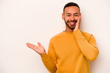 Beyaz arka planda izole edilmiş genç İspanyol bir adam avuç içinde fotokopi alanı tutuyor, el üstünde tutuyor. Şaşırmış ve mutlu..