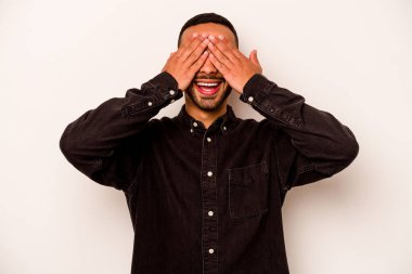 Beyaz arka planda izole edilmiş genç İspanyol adam elleriyle gözlerini kapatıyor, geniş bir gülümsemeyle bir sürpriz bekliyor..