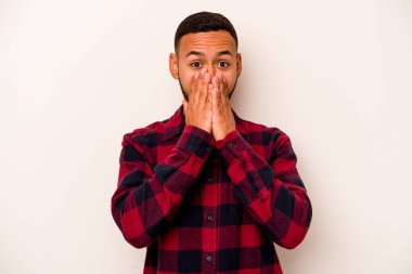 Beyaz arka planda izole edilmiş genç İspanyol adam elleriyle ağzını kapatırken şok oldu..