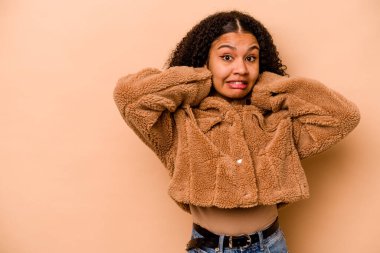 Genç Afrikalı Amerikalı kadın bej arka planda izole edilmiş kafasının arkasına dokunuyor, düşünüyor ve bir seçim yapıyor..