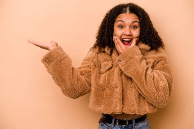 Bej arka planda izole edilmiş genç Afrikalı Amerikalı kadın avuç içinde fotokopi alanı tutuyor, el üstünde tutuyor. Şaşırmış ve mutlu..