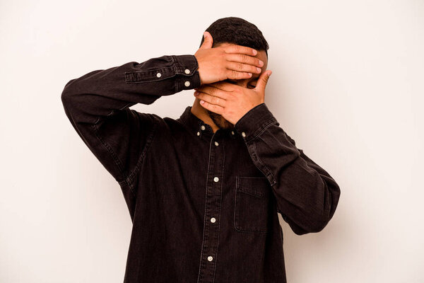 Young hispanic man isolated on white background blink at the camera through fingers, embarrassed covering face.