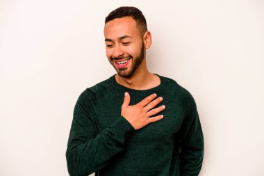 Beyaz arka planda izole olmuş genç İspanyol adam gülüyor, elleri yüreğinde, mutluluk kavramında..