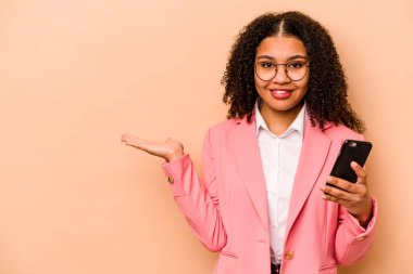 Bej arka planda cep telefonu tutan genç Afrikalı Amerikalı kadın bir avuç içinde fotokopi alanı olduğunu ve diğer elini belinde tuttuğunu gösteriyor..