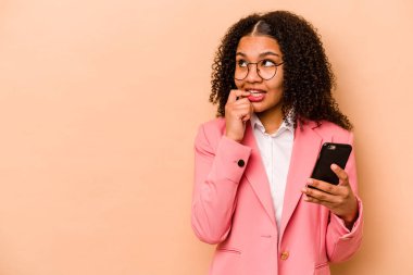 Elinde cep telefonu olan genç Afrikalı bir kadın. Bej arka planda izole edilmiş. Bir şeyin fotokopi odasına baktığını düşünerek rahatlamış..
