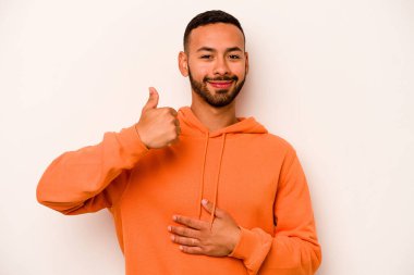 Beyaz arka planda izole edilmiş genç İspanyol adam karnına dokunuyor, nazikçe gülümsüyor, yemek yiyor ve tatmin oluyor..