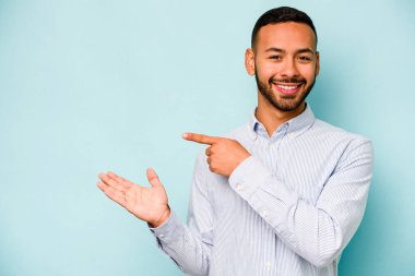 Mavi arka planda izole edilmiş genç İspanyol bir adam heyecanlı bir şekilde avuç içinde bir kopyasını tutuyor..