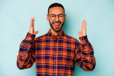 Latin kökenli genç bir adam mavi arka planda zaferi ya da başarıyı kutlarken şaşırmış ve şok olmuştu..