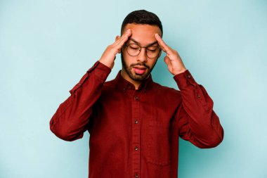 Genç İspanyol adam mavi arka planda izole edilmiş tapınaklara dokunuyor ve baş ağrısı çekiyor..